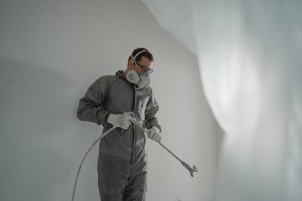 Person in protective gear painting a wall, showcasing house renovation work.